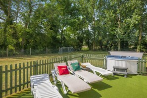 En trädgård med en bubbelpool, solstolar och ett staket av trä.