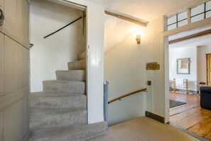 Eine Treppe mit Handlauf, die zu einem Bereich im zweiten Stock mit Holzboden und einer Wandleuchte führt.