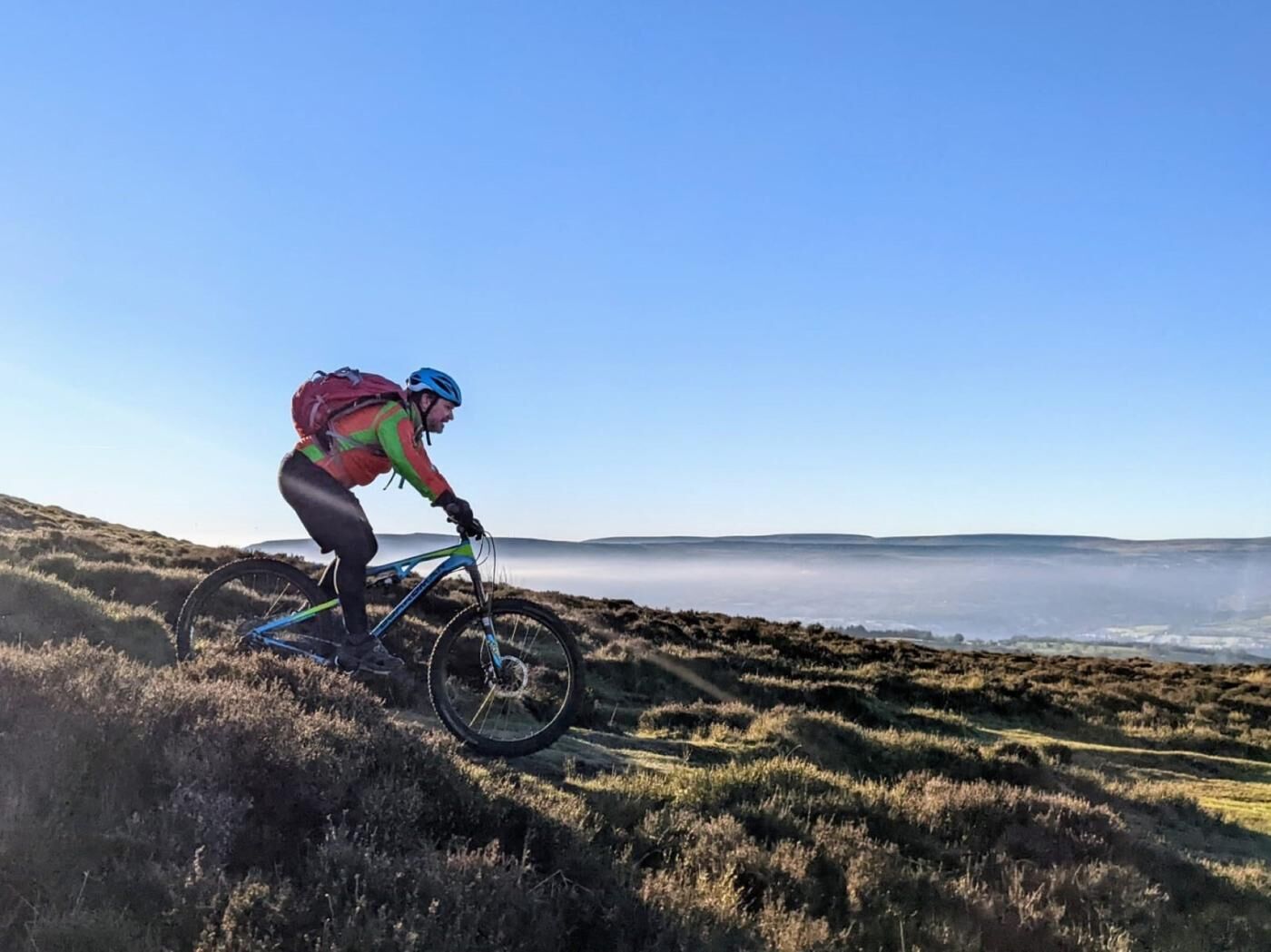 A person riding a mountain bike on a grassy hill with a clear sky.