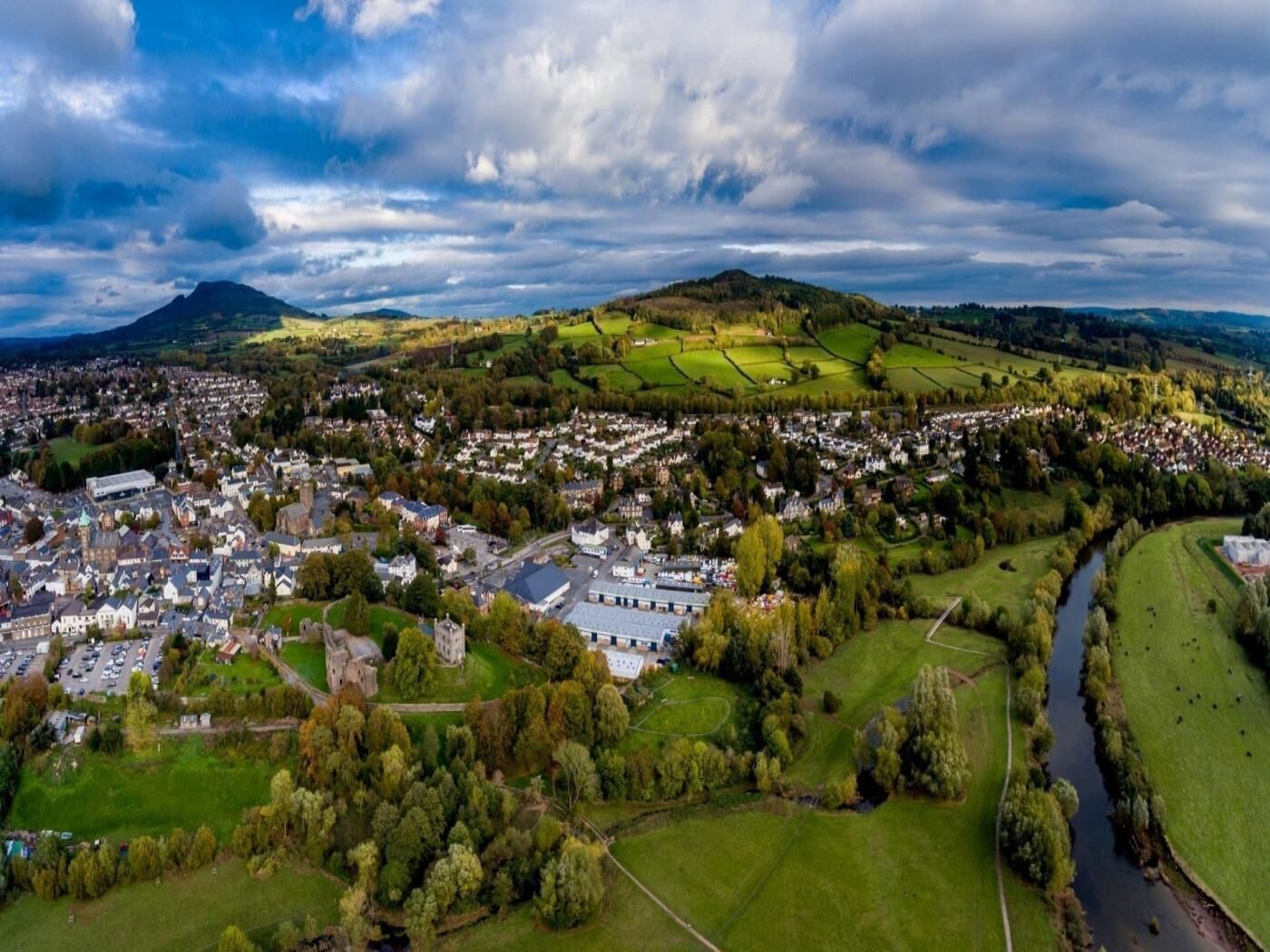 Une vue aérienne d’une ville avec un château imposant, des champs verdoyants et une rivière.