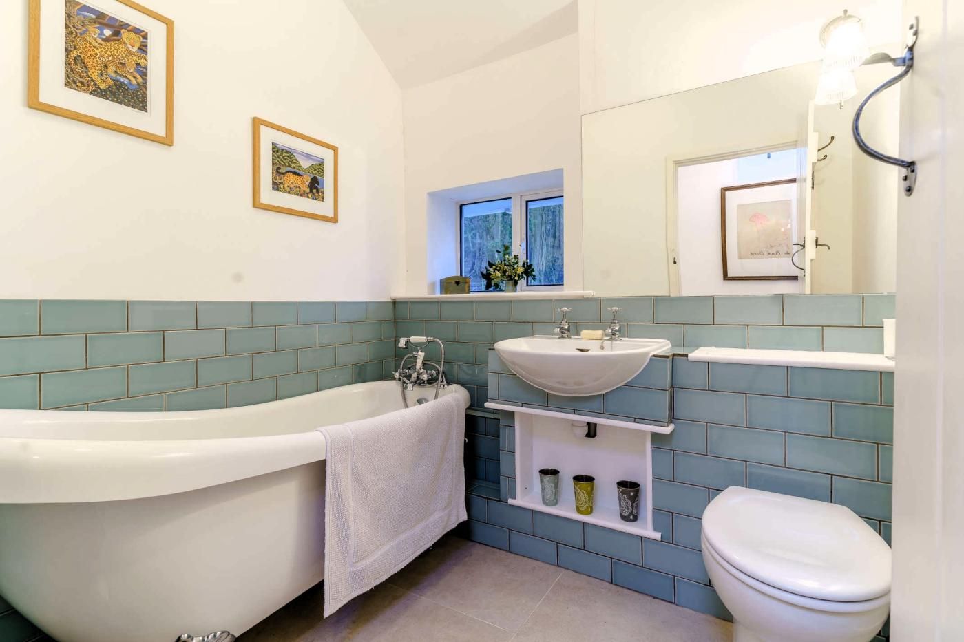 Une salle de bain avec une baignoire sur pieds, un lavabo et des toilettes. Deux tableaux encadrés sont accrochés au mur.