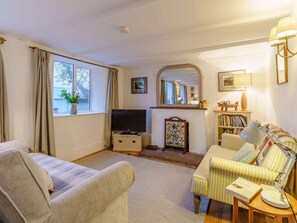 Ein Wohnzimmer mit Sofa, Sesseln, Fernseher, Bücherregal und Kamin.