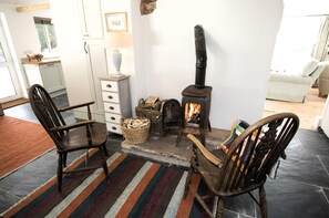 A cozy living room with a fireplace, two wooden chairs, a patterned rug, and a white cabinet. - 4 Bed in Monmouth (oc-42868) (Cwmcarvan)