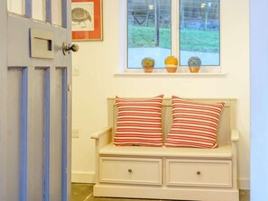 Ein Zimmer mit einer weißen Bank, gestreifter Dekokissen, einer Tür mit blauer Zierleiste und einem Fenster mit drei Vasen auf dem Sims.