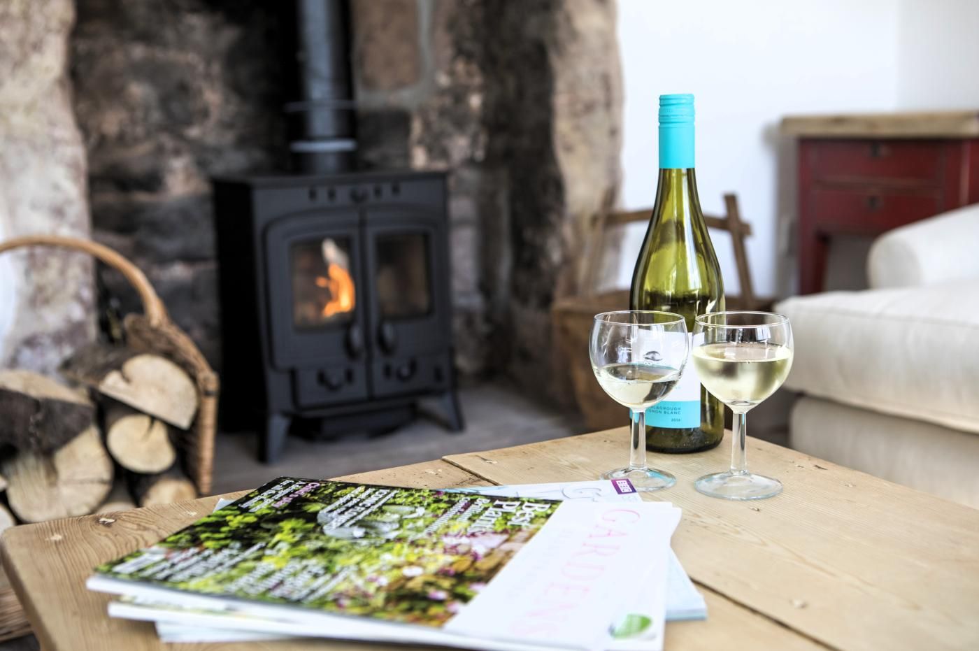 A wooden table with a bottle of white wine, two glasses, and a magazine.