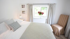 A bedroom with a bed, a chair, a window with curtains, and a vase with flowers. - 4 Bed in Monmouth (oc-42868) (Cwmcarvan)