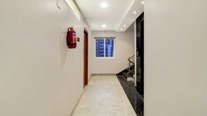 A hallway with a fire extinguisher, a window, and a staircase. - Classic Hotel Didar House (Navi Mumbai)