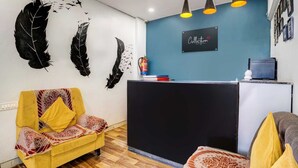 A reception area with a desk, a yellow armchair, and feather wall art. - Classic Hotel Didar House (Navi Mumbai)