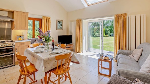 A spacious living area with a dining table, sofa, kitchen, and a large sliding glass door to a garden. - 2 Bed in Conwy (oc-42573) (Ty'n-y-groes)