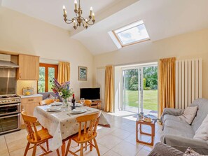 A spacious living area with a dining table, sofa, kitchen, and a large sliding glass door to a garden. - 2 Bed in Conwy (oc-42573) (Ty'n-y-groes)