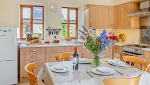 A kitchen with wooden cabinets, a refrigerator, a dining table set for four, and a clock on the wall. - 2 Bed in Conwy (oc-42573) (Ty'n-y-groes)