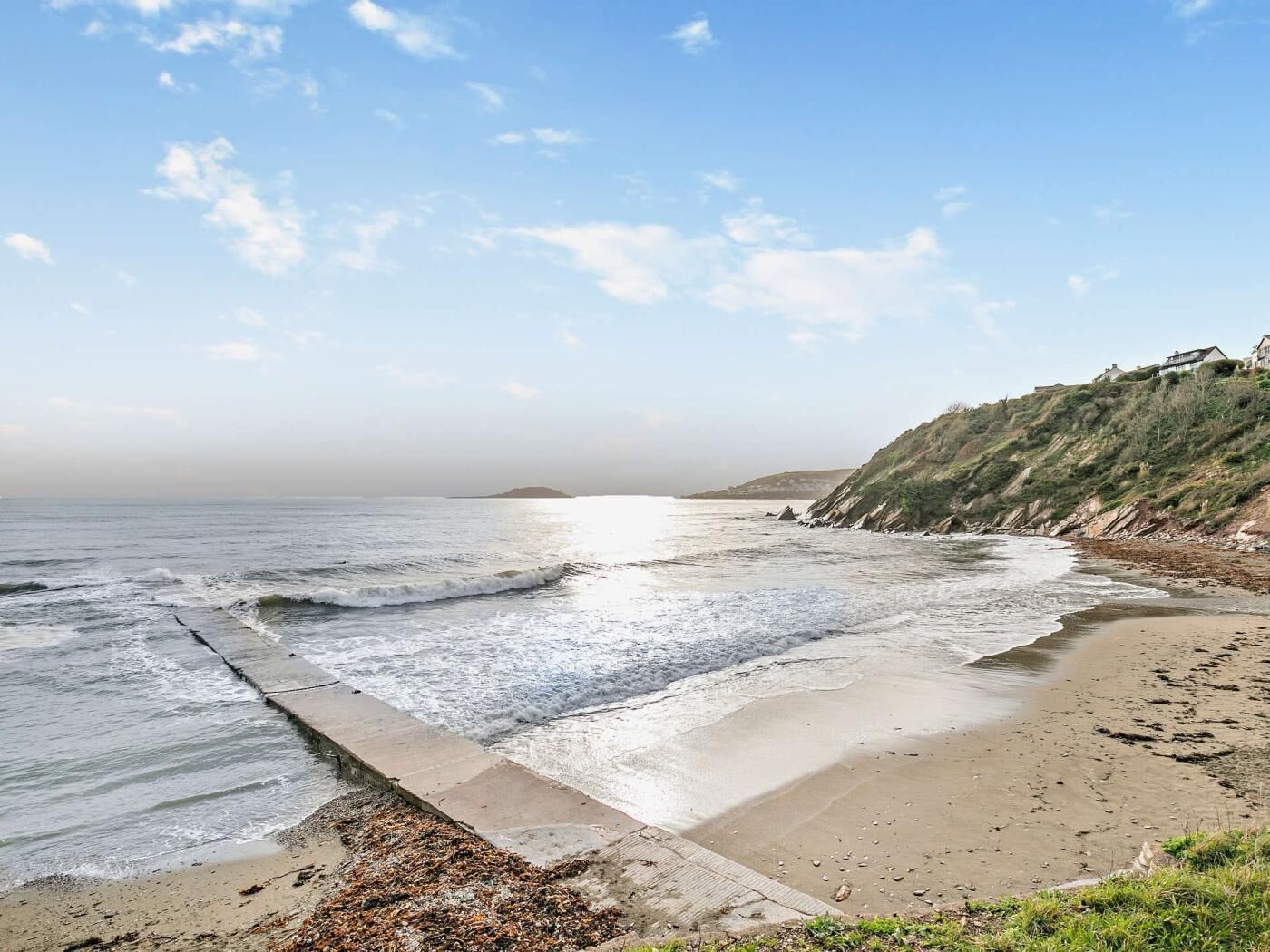A beach with a concrete barrier, sandy shore, and a hill with buildings.