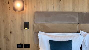Une chambre avec un mur en bois, un lit avec des oreillers blancs et bleu foncé, une table de chevet et un luminaire suspendu.