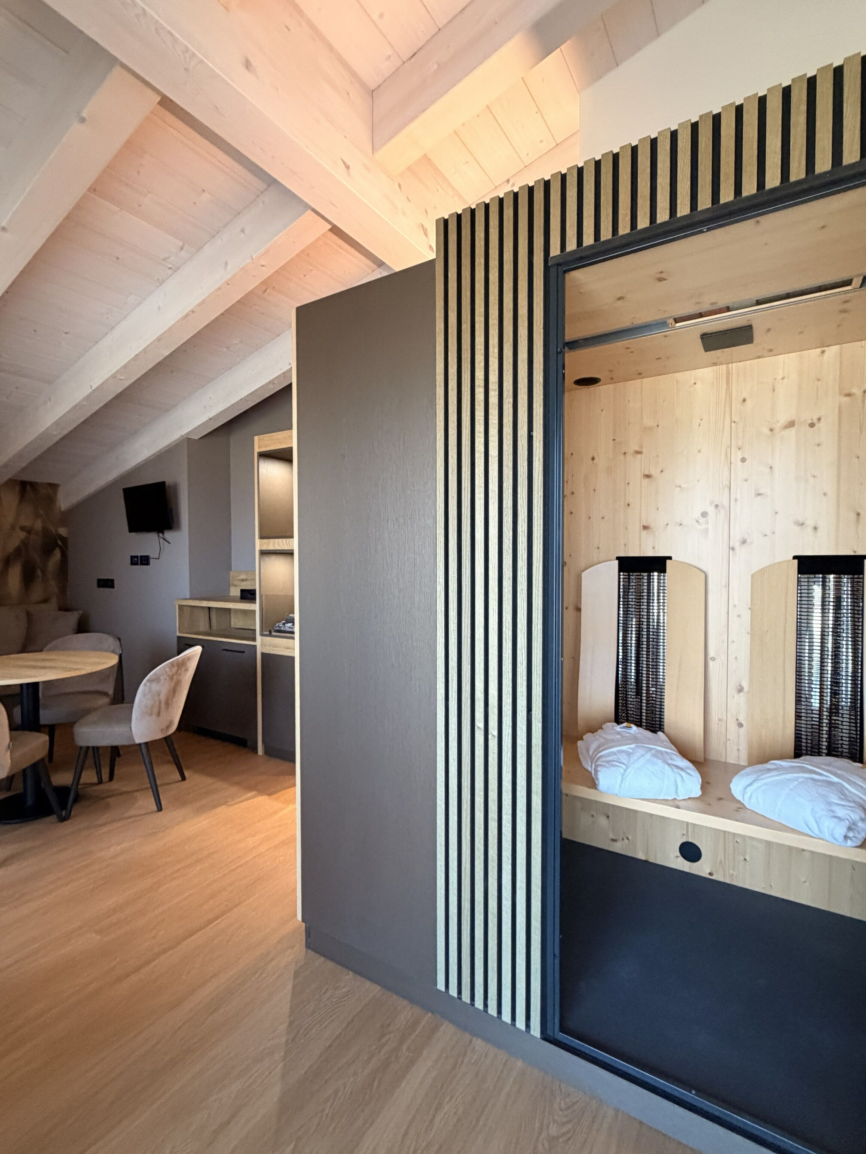 Una habitación moderna con techo de madera, una cama con cabecera, un escritorio con silla y un televisor en la pared.