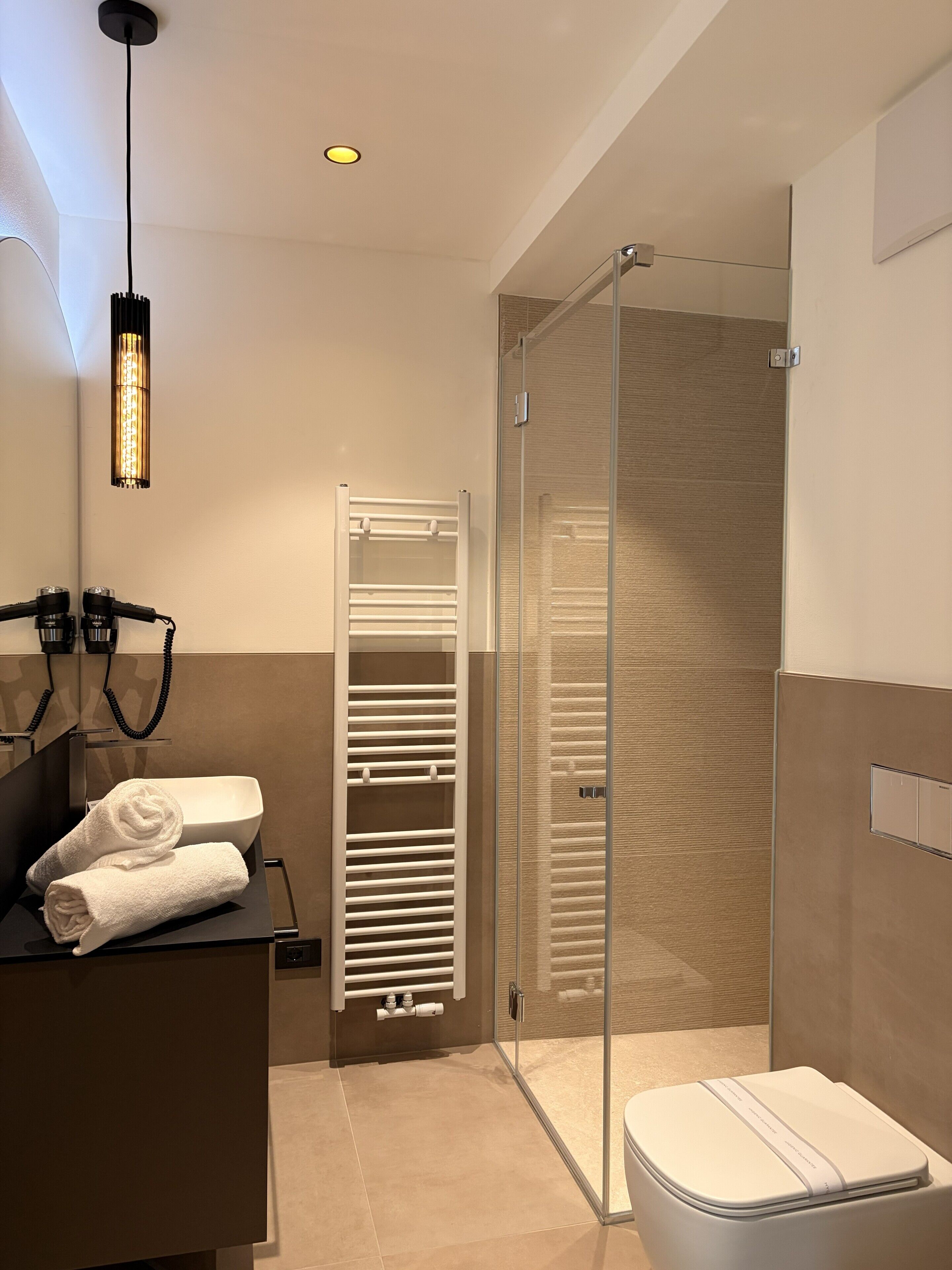 Une salle de bain moderne avec une douche à parois de verre, des toilettes blanches et un porte-serviettes.