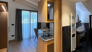 A modern interior with a wooden accent wall, a glass-top table with a decorative item, a built-in sink, and a view through a glass door. - ALPEN RELAIS (Fondo)