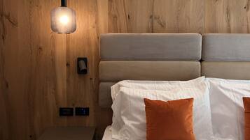 Ett modernt sovrum med en väggpanel i trä, en säng med vita och orange kuddar, ett sängbord och en hängande lampa.