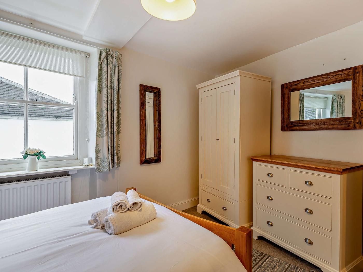 A bedroom with a bed, a wardrobe, a dresser, a mirror, and a window with curtains.