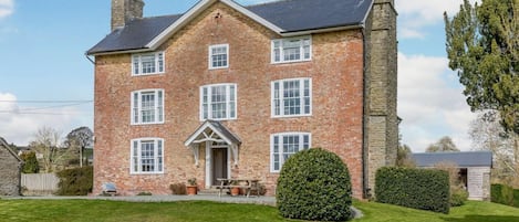 Une grande maison en briques avec une entrée centrale, de nombreuses fenêtres et une cheminée.