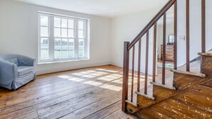 Ein Zimmer mit großem Fenster, Holzboden, einem Sessel und einer Treppe.
