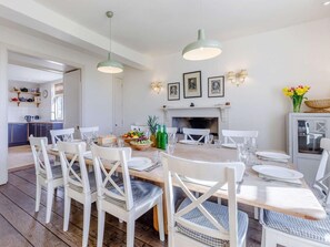 A dining area with a long wooden table, white chairs, and a fireplace. - 8 Bed in Kington (oc-42962) (Titley)