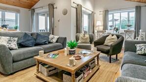 Een moderne woonkamer met een houten plafond, grijze banken, een salontafel en een uitzicht door grote ramen.