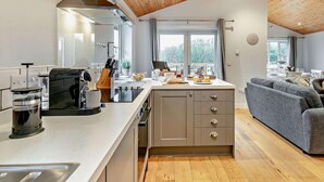 Een moderne keuken met een centraal eiland, houten plafond en een zithoek met een grijze bank.
