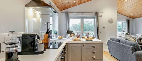 A modern kitchen with a central island, wooden ceiling, and a dining area with a grey sofa.