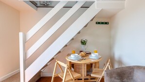 A dining area with a wooden table and chairs, a vase with flowers, and a staircase. - 1 Bed in Okehampton (oc-42982) (Petrockstow)