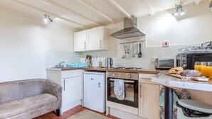 A compact kitchen with white cabinets, a built-in oven, a small refrigerator, and a dining area with a table and chairs. - 1 Bed in Okehampton (oc-42982) (Petrockstow)