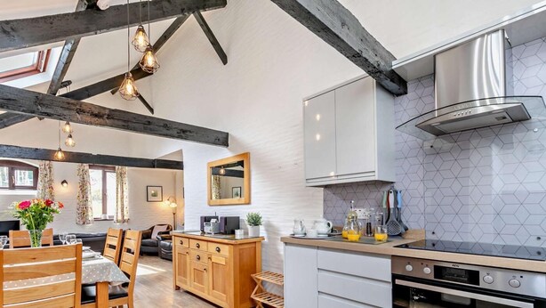 A modern kitchen with wooden cabinets, a built-in oven, and a dining area with a wooden table and chairs. - 3 Bed in Looe (oc-43128) (Saint Martin-by-Looe)