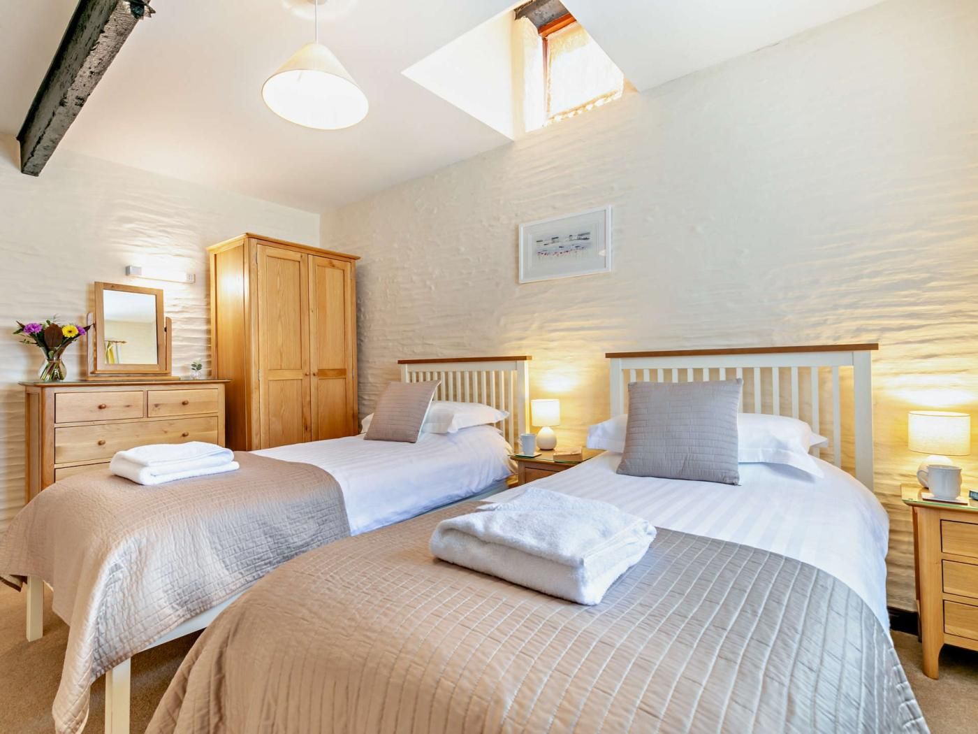 Een hotelkamer met twee bedden, een houten garderobe, een spiegel en een wandlamp.