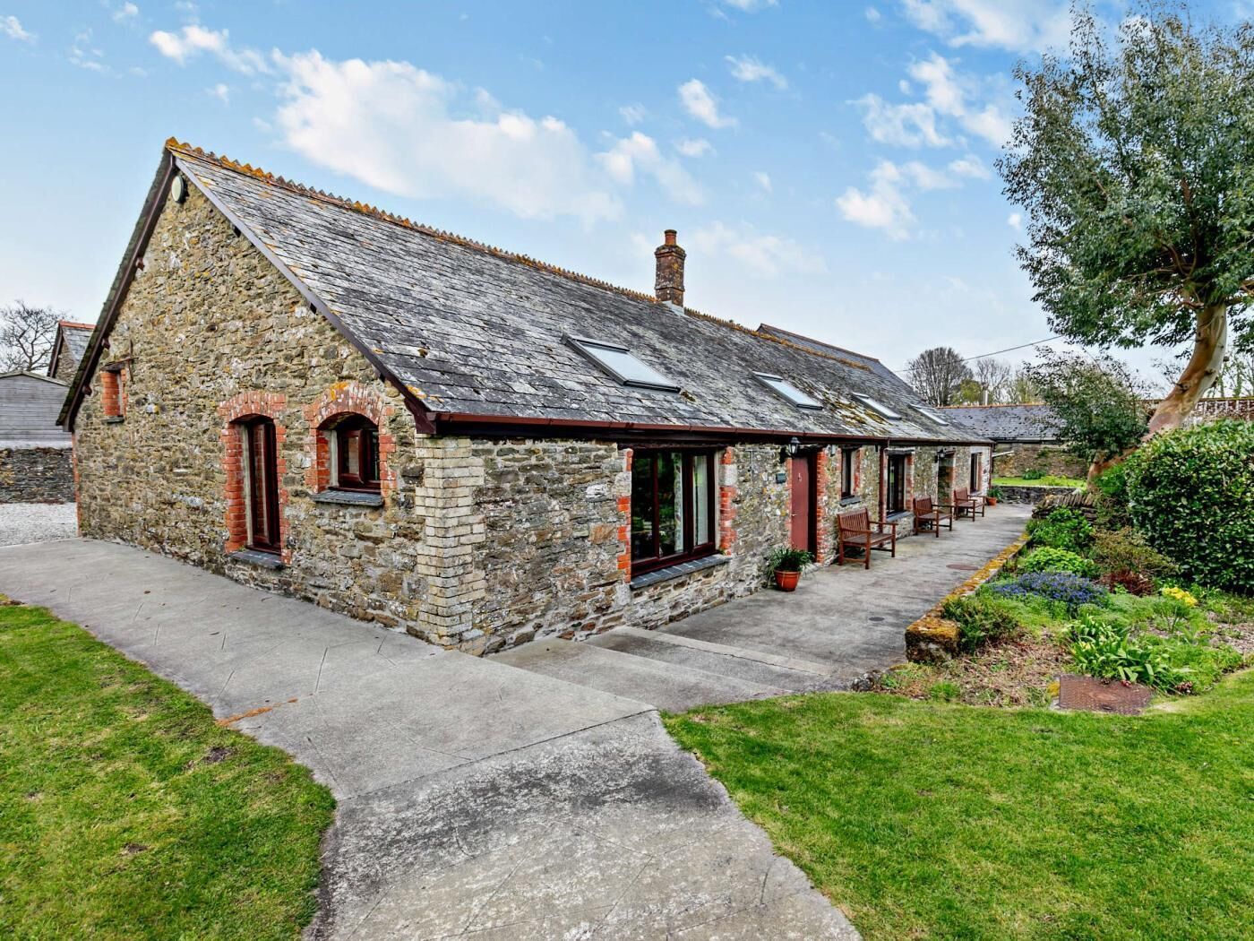 A stone building with a sloped roof, a chimney, and a small porch with chairs.