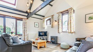 A cozy living room with leather sofas, a wooden coffee table, a television, and a wood-burning stove. - 3 Bed in Looe (oc-43128) (Saint Martin-by-Looe)