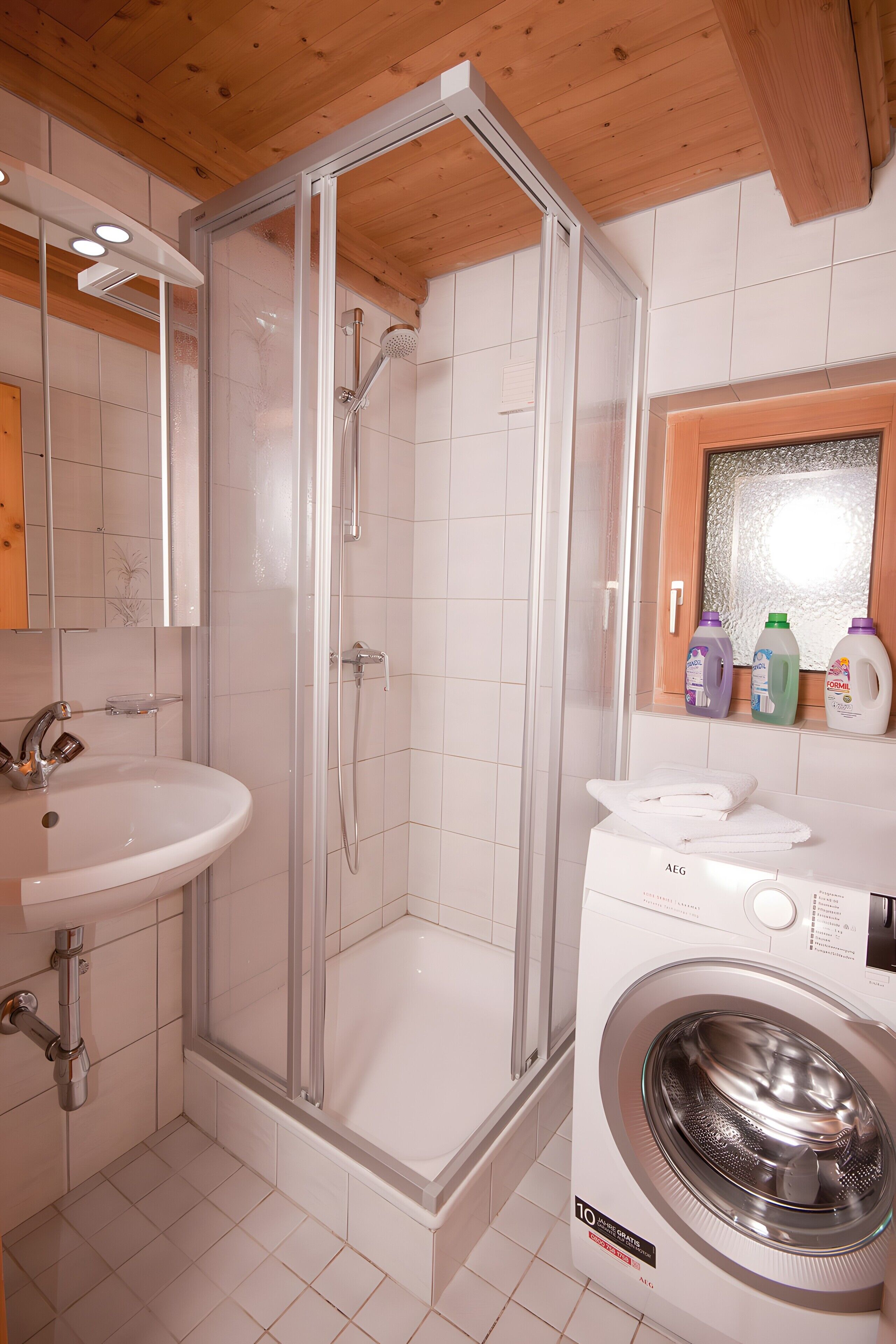 Ein modernes Badezimmer mit einer gläsernen Duschkabine, einem Waschbecken und einer Waschmaschine.