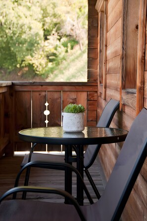 A wooden deck with a table and two chairs, a potted plant, and a view of greenery.