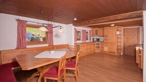 A wooden dining table with chairs, a bench, and a kitchen area with wooden cabinets and a microwave.