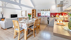 Une cuisine moderne dotée d’un îlot central, un coin repas avec une table pour quatre personnes, et un espace de vie chaleureux avec un canapé et une cheminée.