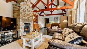 Una sala de estar acogedora con chimenea de piedra, vigas de madera, un sofá de cuero y un televisor.