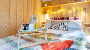 A cozy bedroom with a wooden headboard, a bed with floral pillows, a bedside table with bottles, and a colorful blanket.