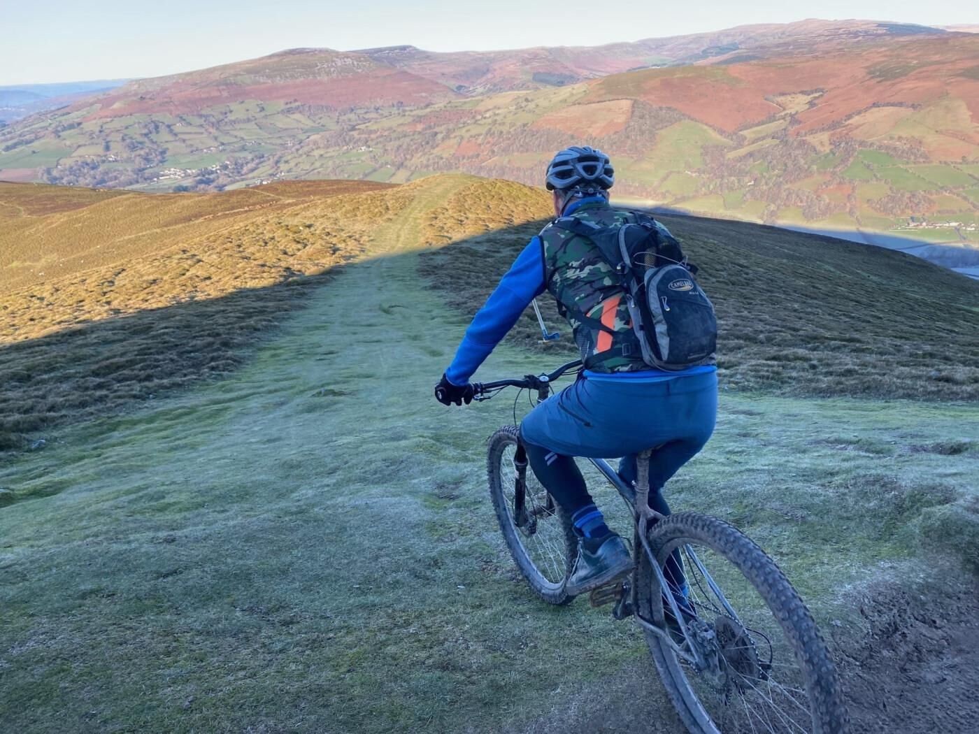 A person riding a mountain bike on a grassy hill with a scenic view of rolling hills in the background.