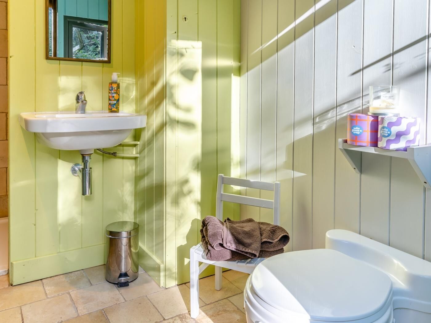 A bathroom with a white sink, a toilet, a trash bin, and a chair with towels.