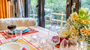 A dining table set with plates, cutlery, glasses, and candles, with a view of greenery outside.