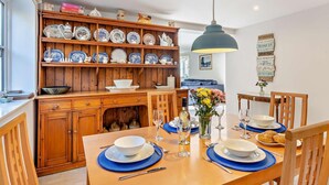 Ein Essbereich mit einem Holztisch, gedeckt für vier Personen, umgeben von Stühlen. Im Hintergrund ist ein Holzschrank mit Geschirr zu sehen.