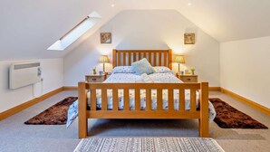 Ein Schlafzimmer mit schrägen Wänden, einem hölzernen Bett, zwei Nachttischlampen, einer Heizung und einem Oberlicht.