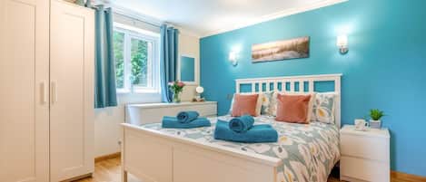A bedroom with a bed, a nightstand, a window with curtains, a wardrobe, and a ceiling light.