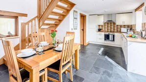 Een moderne keuken met een houten trap, een eethoek met een tafel voor vier personen en uitzicht op de woonkamer.