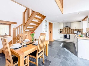 Eine moderne Küche mit einer Holztreppe, einem Essbereich mit Tisch für vier Personen und Blick zum Wohnbereich.