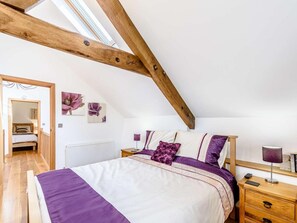 A bedroom with a sloped ceiling, a bed with a purple and white bedspread, a wooden nightstand, and a radiator.