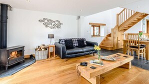 Een moderne woonkamer met een open haard, een zwarte leren bank, een houten salontafel en een trap.
